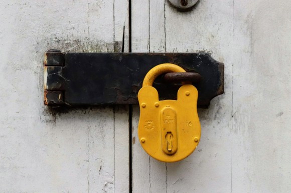 A bright yellow lock against a fades white shed door. I have adopted this as my avatar across my social media sites