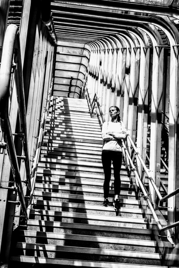 a woman walking down the covered walkway from Gallions Reach DLR station. Sun streaking through the railings creating dramatic patterns