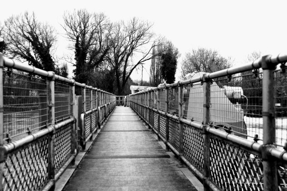 A log view of Caversham weir with its metal railings on both sides narrowing to the bridge entrance