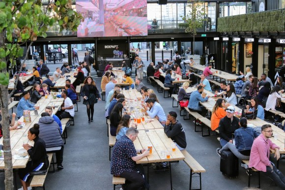 five rows of tressle tables with an array of revelers eating and drinking in groups