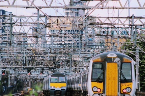 two trains: one coming out of Liverpool Street station and one going in, all underneath an array of overhaed electric cables
