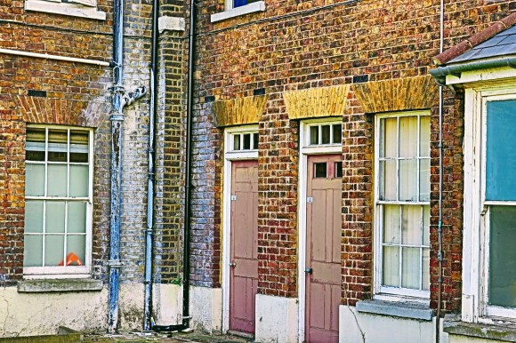 some tired looking doors and windows in a corner of this old hospital with water damage from downpipes on show. The colours are drab which highlights this tired view