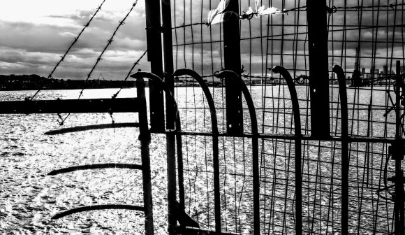 a long distance view of the Thames Barrier through a spiky and wired barrier in the foreground