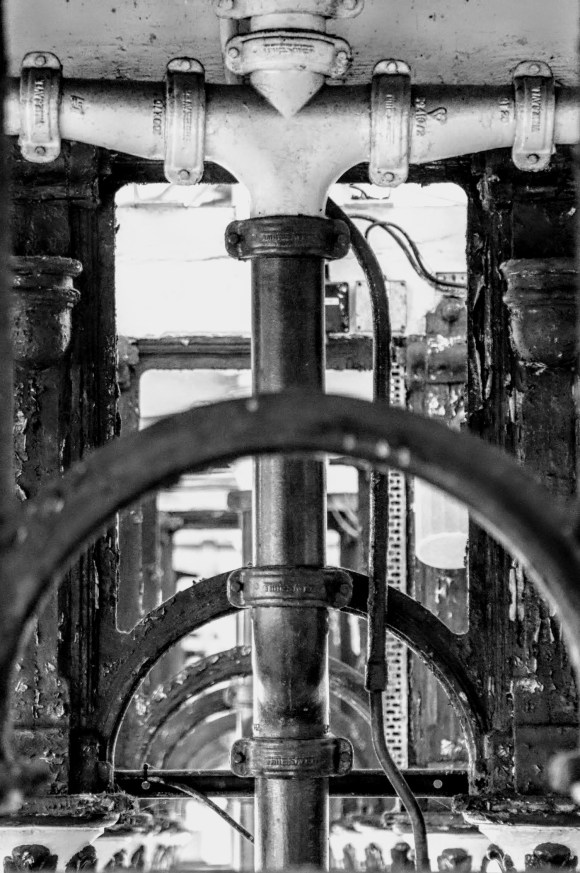 looking up into the roof void of this platform canopy , taken in black and white. the view shows off the symmetrical arched duct work intersected with rainwater down pipes