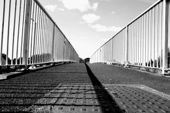 A view looking along the length of a footbridge with railings on either side focusing on a slightly cloudy sky