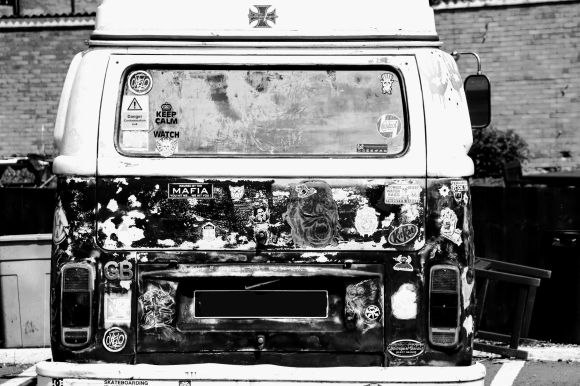 A rear view of a VW campervan covered in a variety of stickers. The image is in black and white
