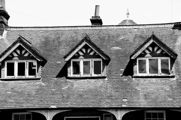 A black and white photo of a view of three dorma windows at roof level on the dilapidated pavillion style building 