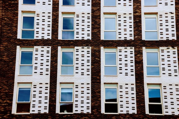 A colour photo of four columns of three vertical windows framed by white vertical bricks dotted with brown bricks to complement the main building brick colour