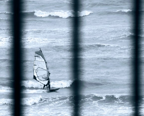 a black and white photo of a windsurfer caught beteen railings