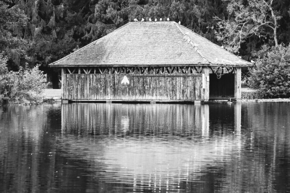 a black and white image of the boathouse in Tredegar Park with it's reflection on the lake's surface