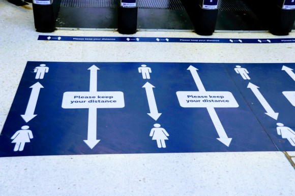 blue floor notices asking passengers to 'please keep your distance'