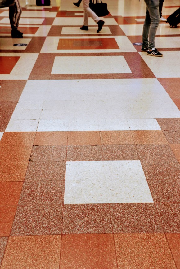 the mosaic floor in the station comprising of brown squares within brown squares in different shades and passengers walking over them