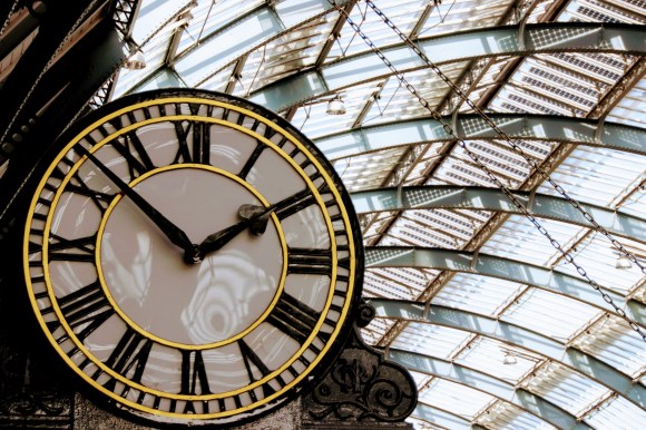 a large gilded station clock with roman numerals. taken from the ground and looking up to the vailuted ceiling