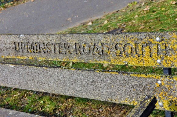 the back panel of a roadside bench with 'Upminster Road South'  engraved into it. The word 'south' is lichen encrusted