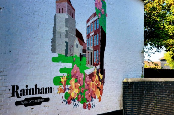 A wall mural depicring a colourful and idylic scene of the church and hall with a floral foreground