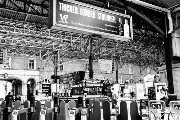 a black and white view over the platform gates into the main concourse devoid of many passengers.