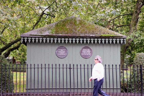 a green painted hut in Dorset Fields with a pedestrian walking past. the hut displays two blue plaques. The left one decalring its unveiling by Colin Codrey, MCC Prsesident, and the one on the right commemorating the site where Thomas Lord laid out his original cricket ground in 1787