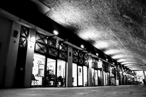 black and white 'moody' image of the Arches with uplighters highlighting  the curved roof. Shop windows all lit up