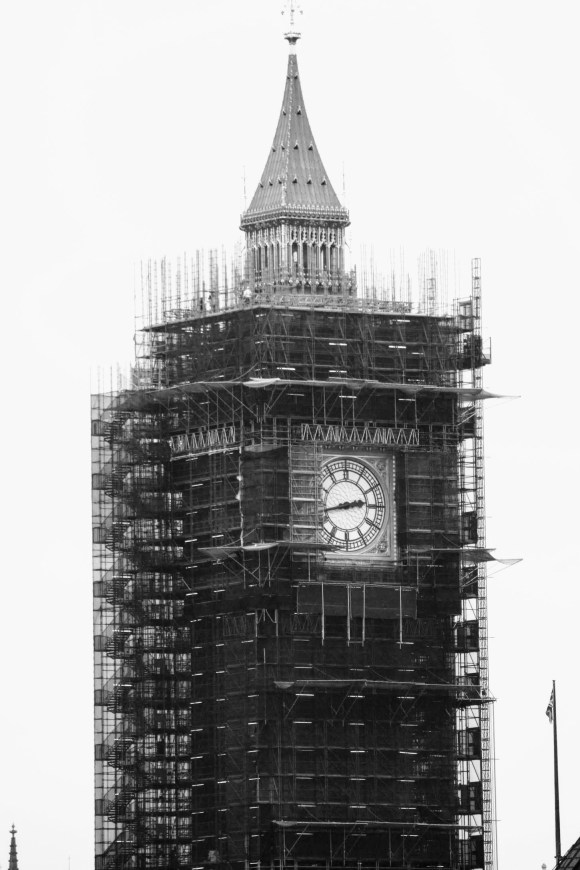 black and white of Big Ben tower encased in scaffolding. The only parts not covered are the clock face and the golden tower