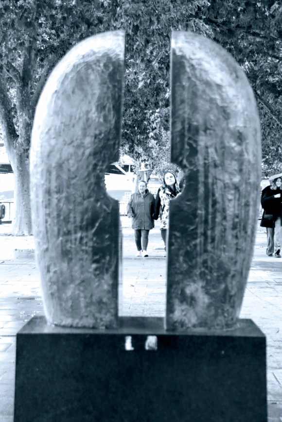 black and white with a blue hue. Two people looking through the sculpture. The best way to describe the sculpture is like a 'bum' (sorry), with a gap.