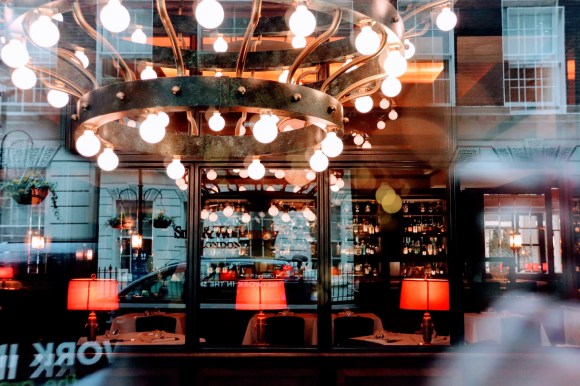 a colour image shot through the wondow of the restaurant. The image is a mixture of the main decorative ceieling and table lights inside, and a view of the buildings on John Adam Street reflected in the window