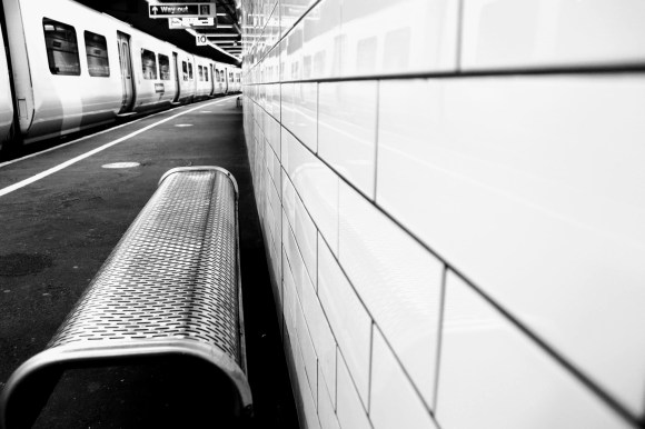 Black & White: looking down platform 10 with three parallel views: from left to right - train standing on the platform; perforated metal seat, and a white tiled wall