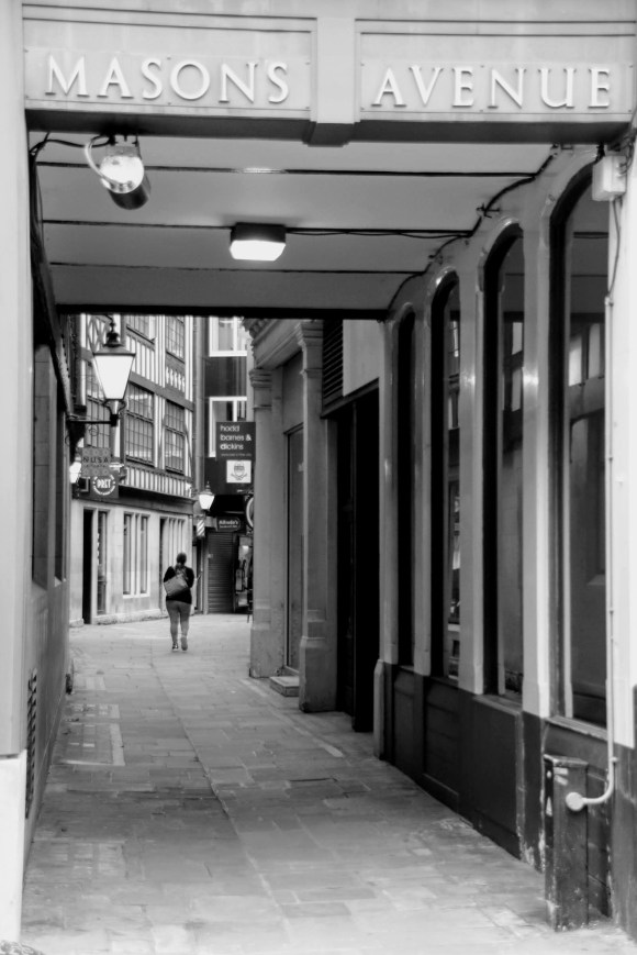 Black & White: looking through the northern entrance to Masons Avenue with its name above the entrance looking through an empty walkway with only one pedestrian