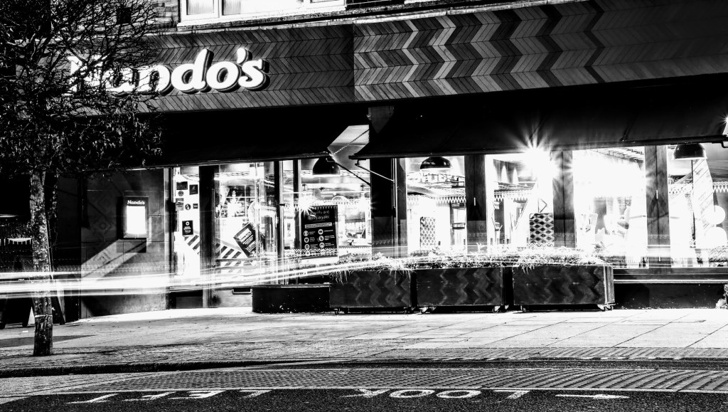 A black and white view of the front of Nando's with their shop windows all lit up